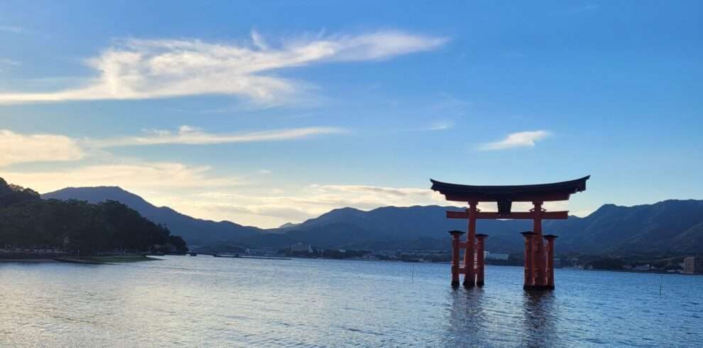 iconic red torii gate with feet submerged in water during sun down at Miyajima near Hiroshima in Japan