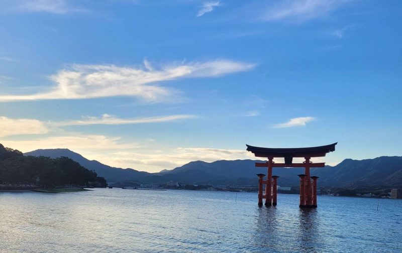 iconic red torii gate with feet submerged in water during sun down at Miyajima near Hiroshima in Japan